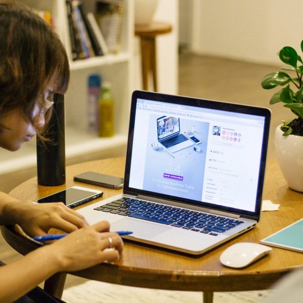 woman in black tank shirt facing a black laptop computer on brown wooden round table